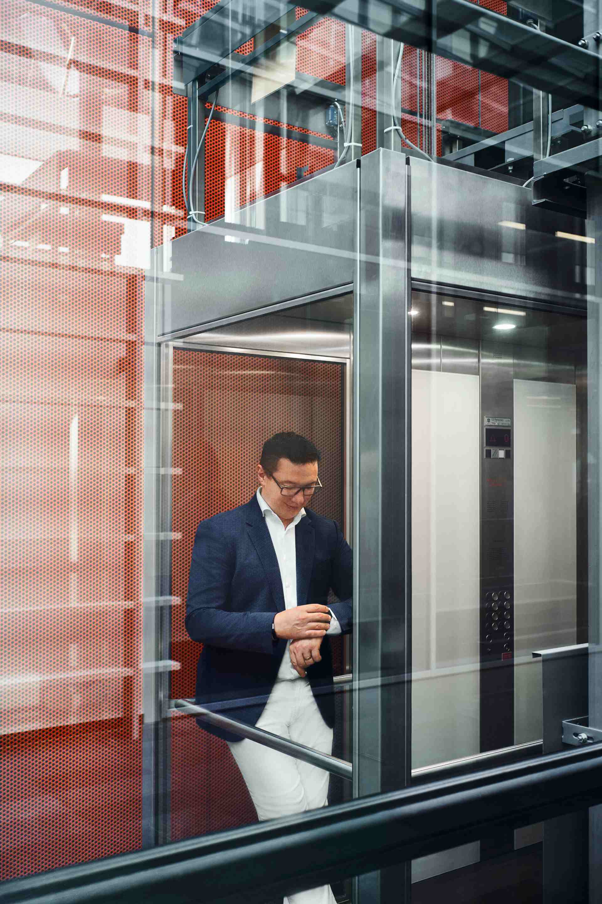 Giorgio Delucchi standing in a glass elevator, looking at his wristwatch.